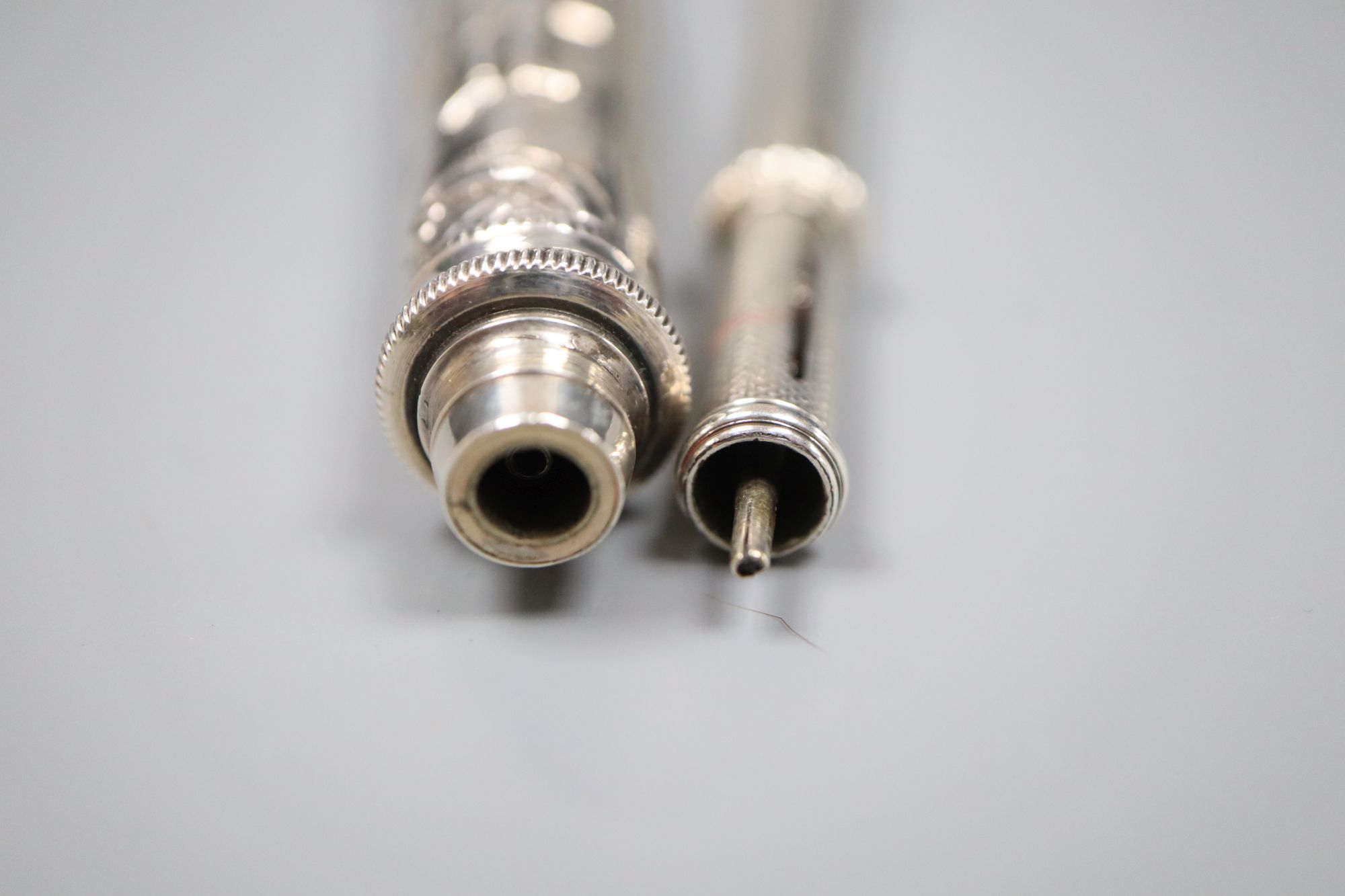 Two white metal propelling pencils, including engine turned with amethyst coloured intaglio set terminal, 93mm.